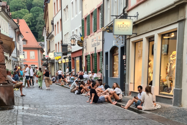Straße mit kleinen Geschäften und Menschen, die auf der Straße sitzen mit den Füßen im Bächle