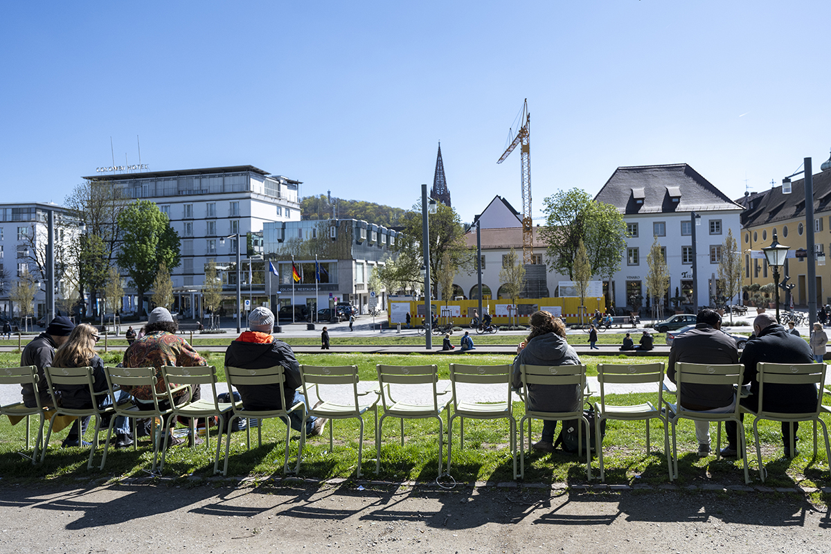 Grüne Stühle auf denen Menschen sitzen, im Hintergrund das Münster und die Freiburger Innenstadt