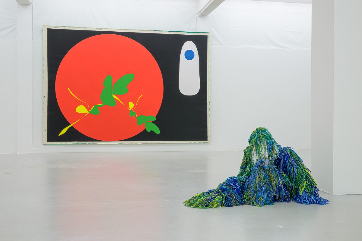Ausstellungsansicht mit einer großen Malerei mit großen roten Kreis von Pia Rosa Dobrowitz und eine kauernde Figur im blau-grünen Tarnanzug von Yongkuk Ko