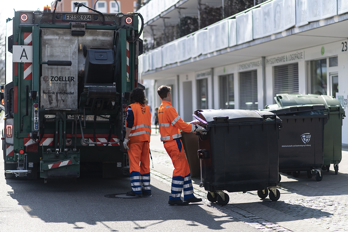 Müllauto mit Mülltonnen und Menschen, die die Mülltonnen bewegen