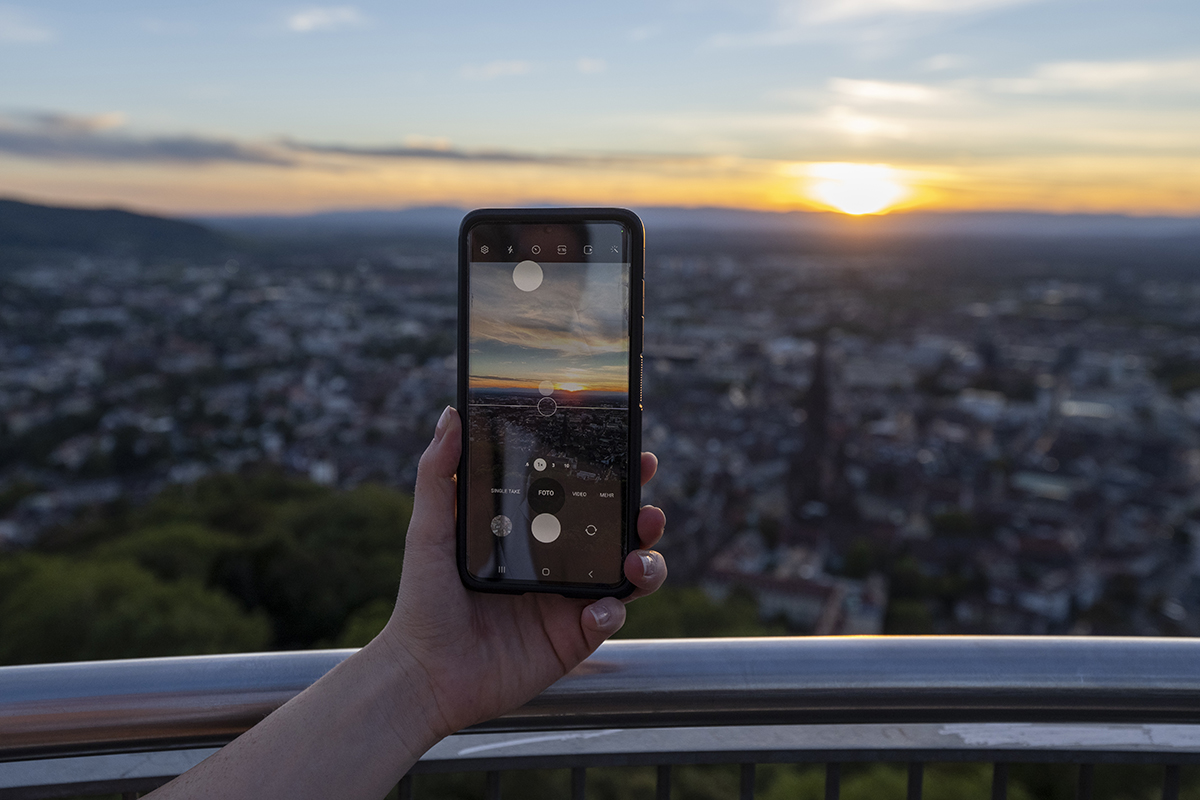 Jemand will mit seinem Handy ein Bild vom Sonnenuntergang über Freiburg machen