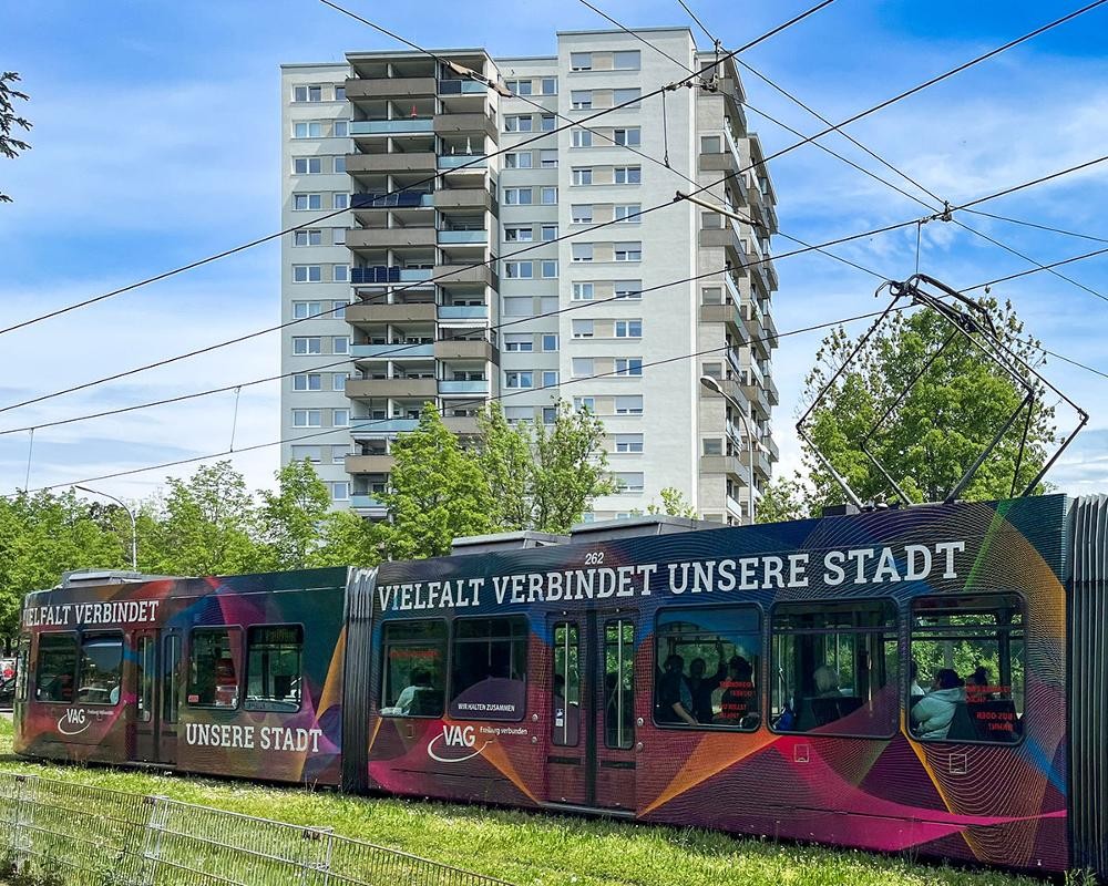 Hochhaus, davor Straßenbahn mit Aufschrift "Vielfalt verbindet unsere Stadt"