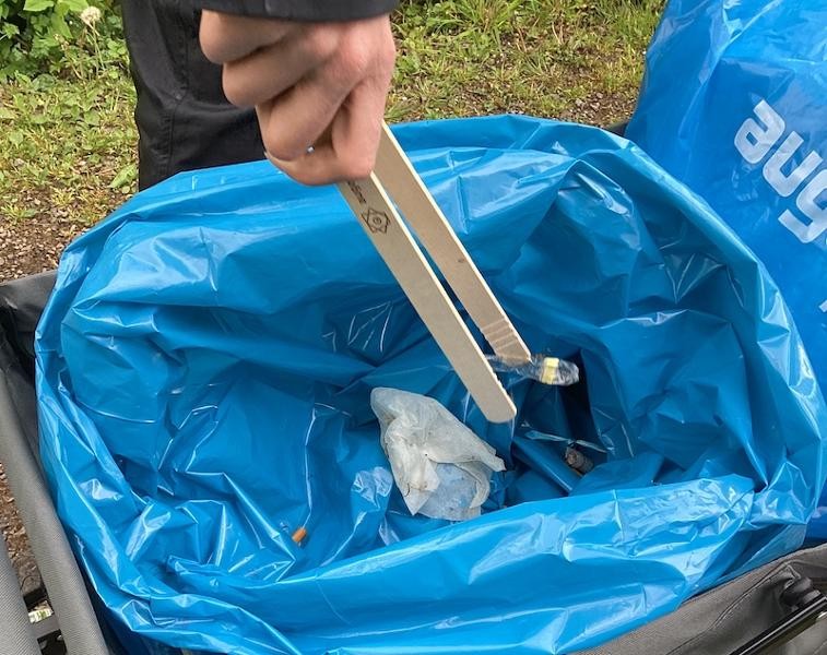 Im Wald wird Müll mit einer Zange gesammelt.