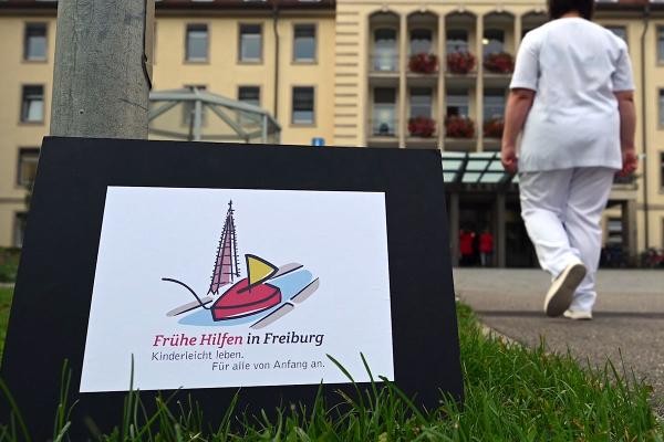 Frau vor der Unikilink neben Schild Frühe Hilfen