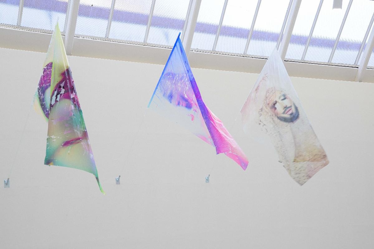 Ausstellungsansicht von "Fields of Un/Rest". drei bunte wehende Fahnen, die an Glasstangen montiert sind