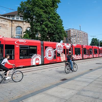 Eine rote Straßenbahn und Radfahrende am Platz der Alten Synagoge