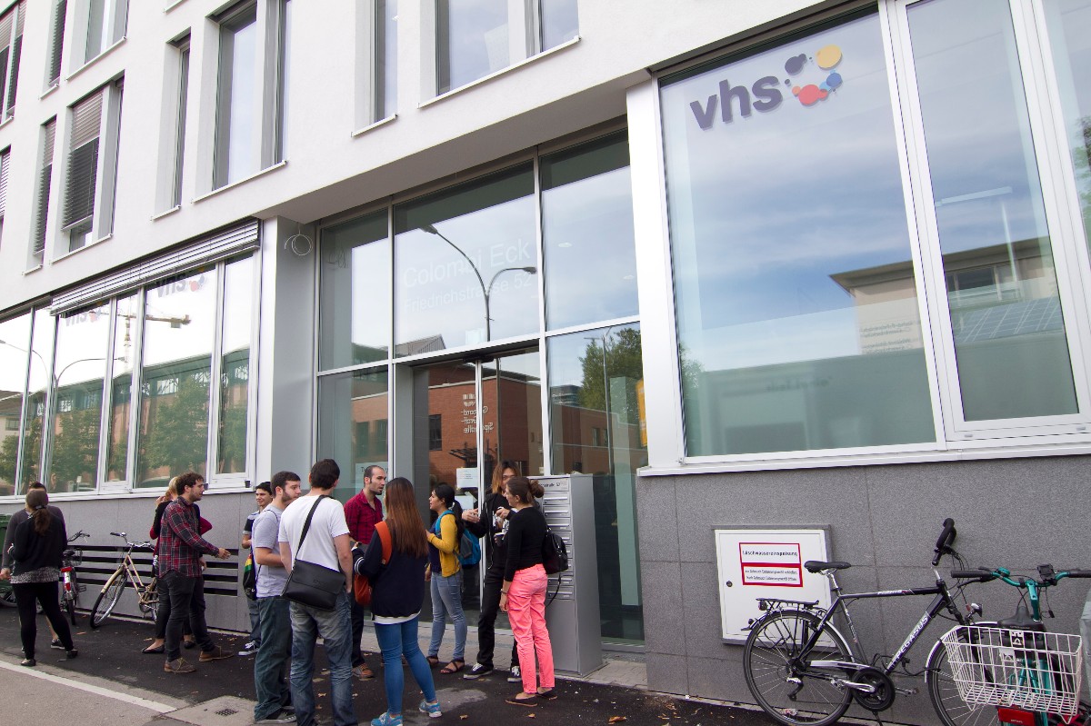 Bild vom Eingang der VHS Freiburg, Menschen stehen davor