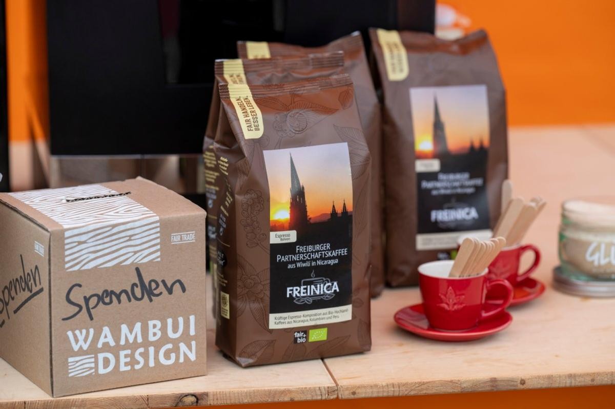 Ein Holztisch, darauf links eine Spendenbox, in der Mitte verpackter Partnerschaftskaffee und rechts Espresso-Tassen.