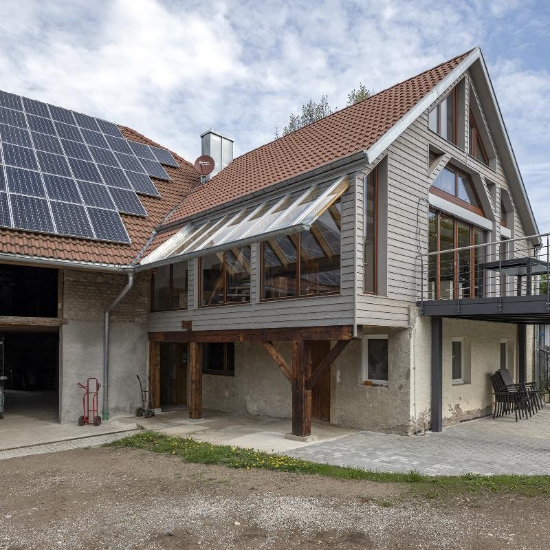 Scheune nach der Sanierung Außenansicht der sanierten Scheune mit Balkon, PV und großzügigen Fensterfronten.