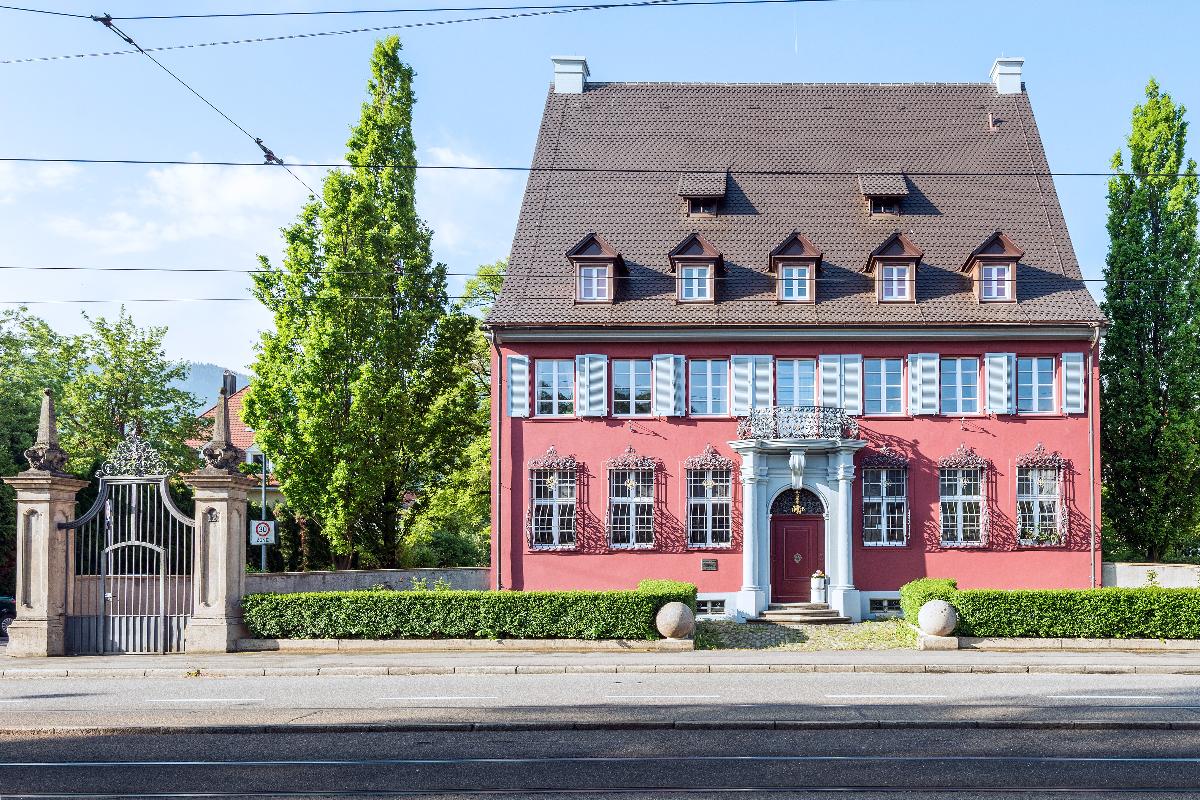Ansicht des renovierten Hauses. Das Haus hat ein neues Dach und die Fassade ist in einem auffälligen Rot gestrichen.
