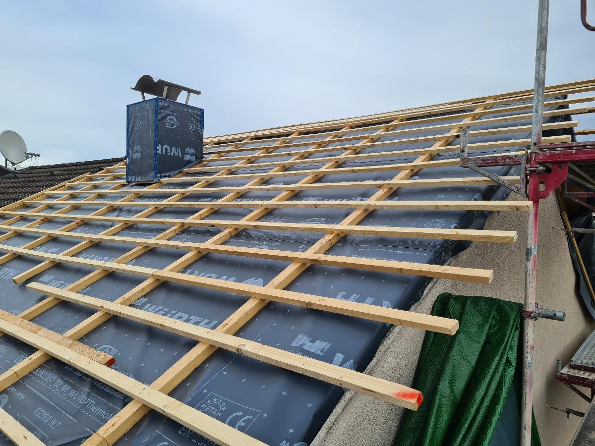 Ein Dach befindet sich in der Sanierung, man sieht die unter den Ziegeln liegende Holzkonstruktion