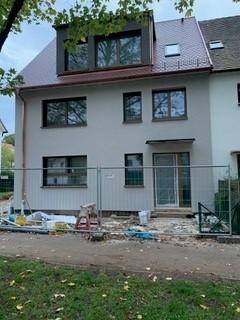Sicht auf das sanierte Haus aus Straßenperspektive. Man sieht die sanierte Fassade, das sanierte Dach und eine ausgebaute Dachgaube