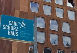 Häuserwand mit vielen Scheiben und einem Schild mit der Aufschrift "Carl-Schulz-Haus"