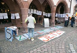 Zwei Personen legen einzelne Buchstaben auf den Boden, die das Wort "Sozialticket jetzt" ergeben