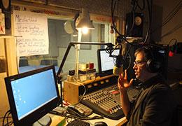 Ein Mann in einem Radiostudio mit PCs, einem Mikrofon und einem Mischgerät