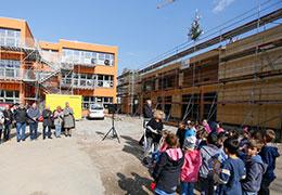 Schulklasse im Freien vor zwei Gebäuden die umgebaut werden