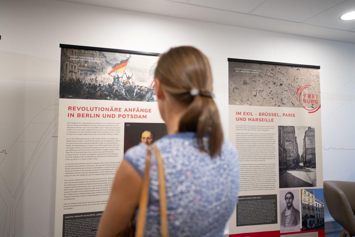 Frau blickt auf Infotafeln zur Ausstellung über Maximilian Dortu