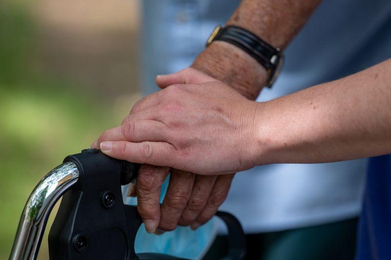 Eine Hand liegt auf einer anderen Hand, die einen Rollatorgriff hält