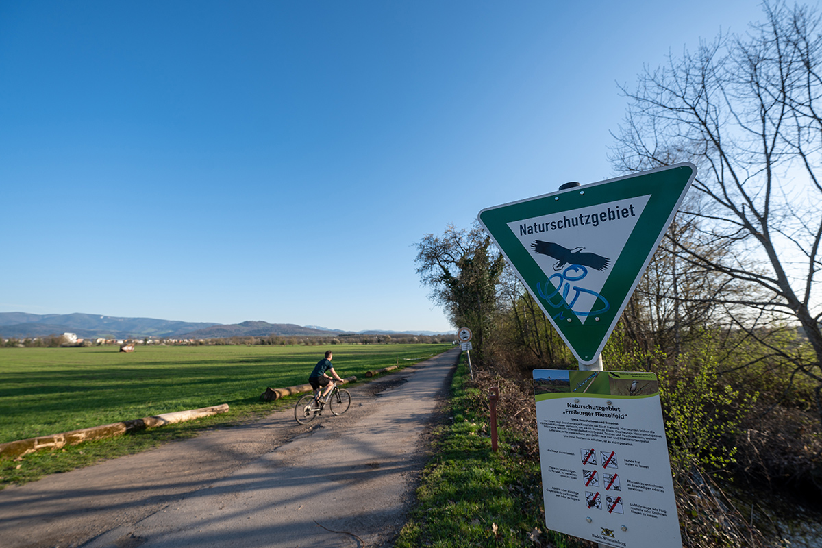 Schild "Naturschutzgebiet" vor einer Wiese mir Weg