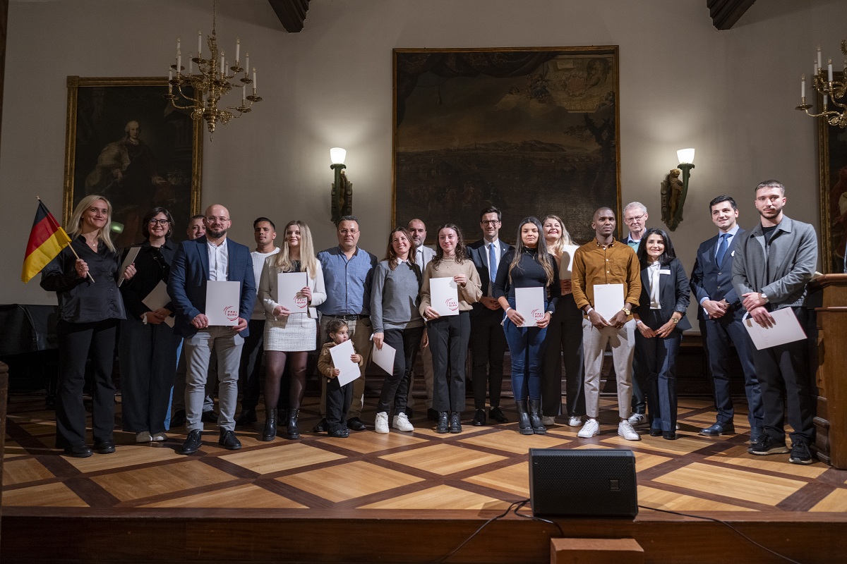 Eine Gruppe der neuen Staatsbürger*innen im historischen Kaufhaus in Freiburg, sie halten ihre Urkunden in der Hand, eine hält eine Deutschlandfahne