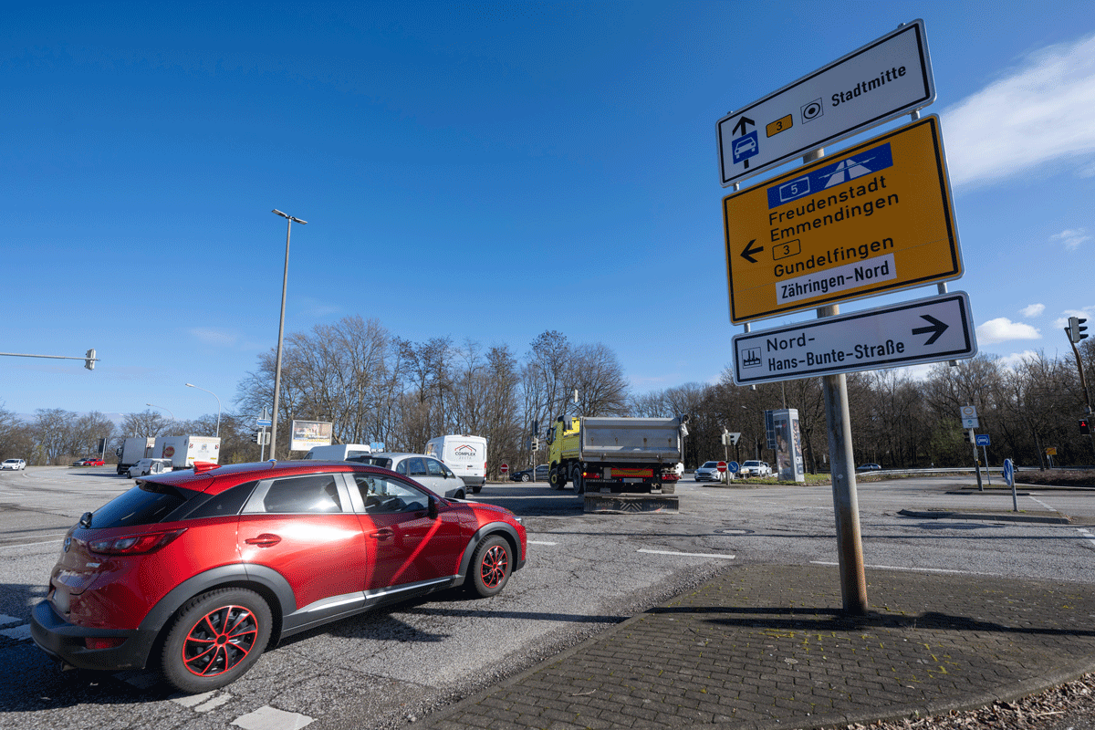Eine befahrene Kreuzung auf der Mooswald-Allee, im Vorder-Grund Weg-Weiser