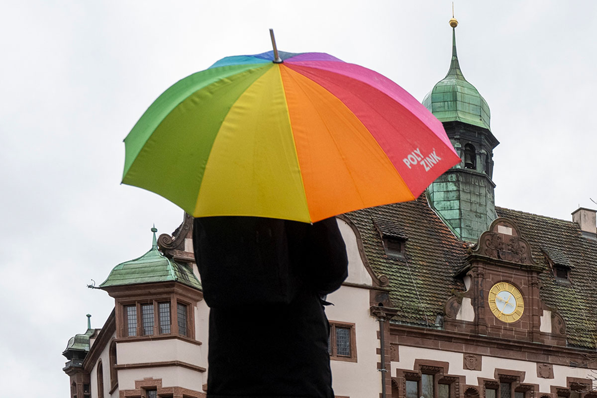 Person von hinten mit buntem Regenschirm vor dem Neuen Rathaus in Freiburg