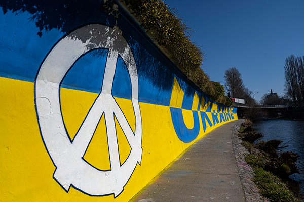 Betonmauer an einem Fluss mit großem Grafitto in blau und gelb mit Peace-Zeichen und Schriftzug "Ukraine"