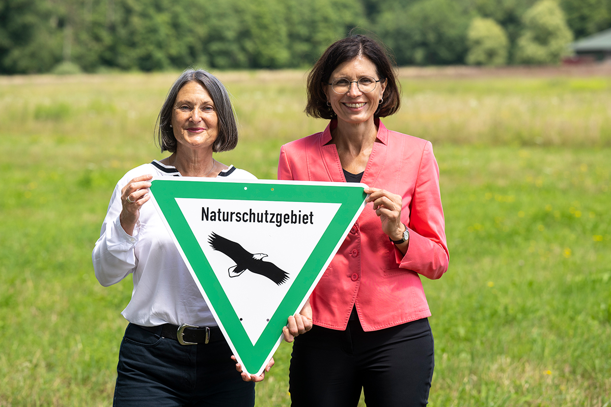 Regierungspräsidentin Bärbel Schäfer und  Bürgermeisterin Christine Buchheit mit einem Hinweisschild „Naturschutzgebiet“.