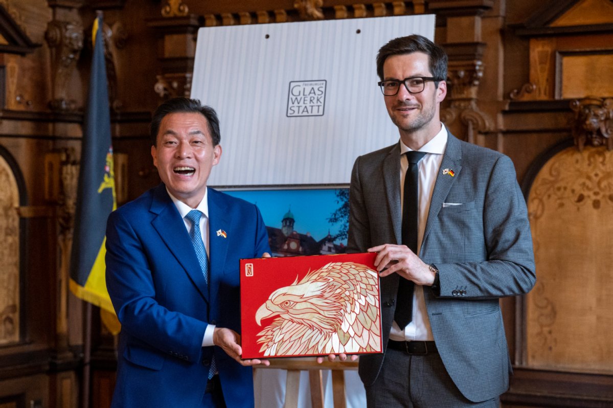 Jea-Joon Lee und Martin Horn halten zusammen im Rathaus ein Bild eines Vogels hoch.