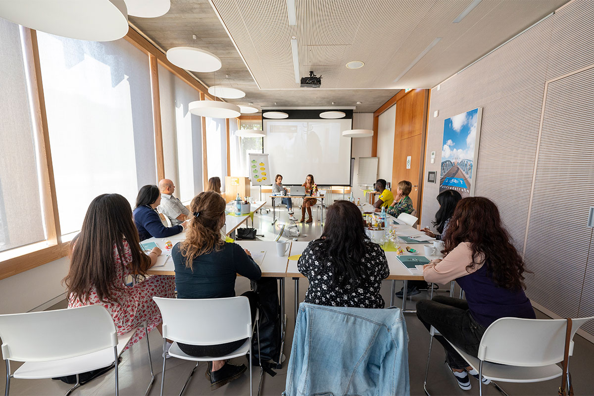 Mehrere Personen in einem Raum um einen U-förmigen Tisch