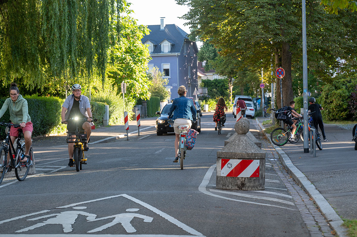 Straße mit Fahrradfahrerinnen, Auto und Fußgängerübergang