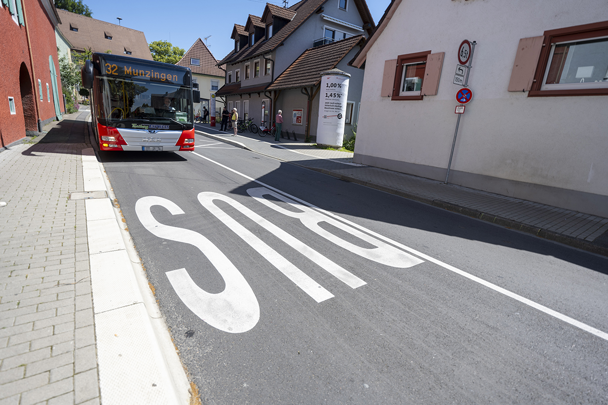 Ein roter VAG-Bus der Linie 32 nach Munzingen steht an der Haltestelle. Auf der Straße ist die Fahrbahn beschriftet mit "BUS".