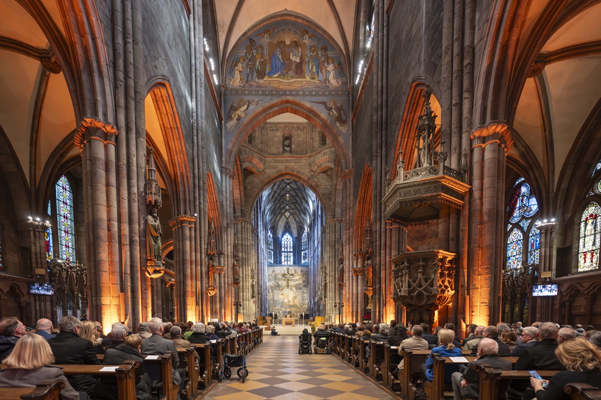 Kirchlicher Teil im Augustinermuseum mit vollen Bänken und orange-roter Beleuchtung.