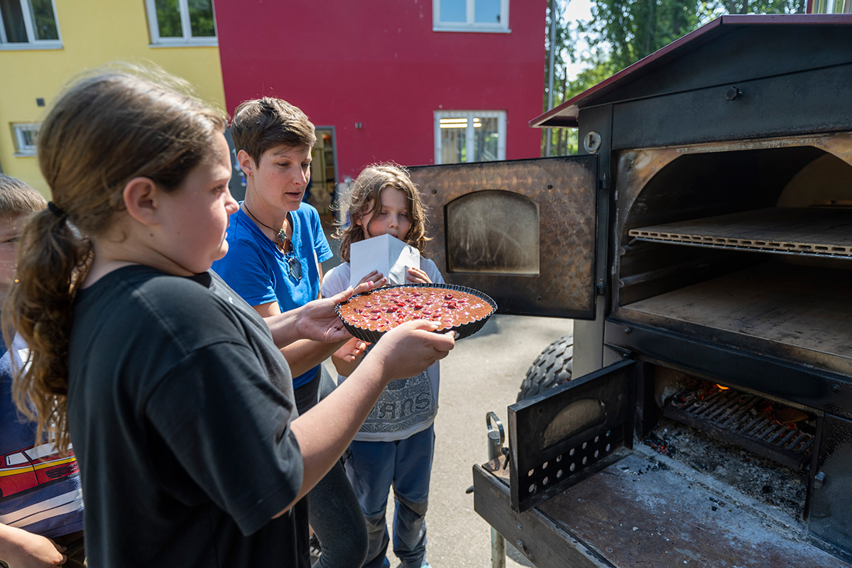 Kinder und Anleiterin schieben einen Kuchen in den Ofen