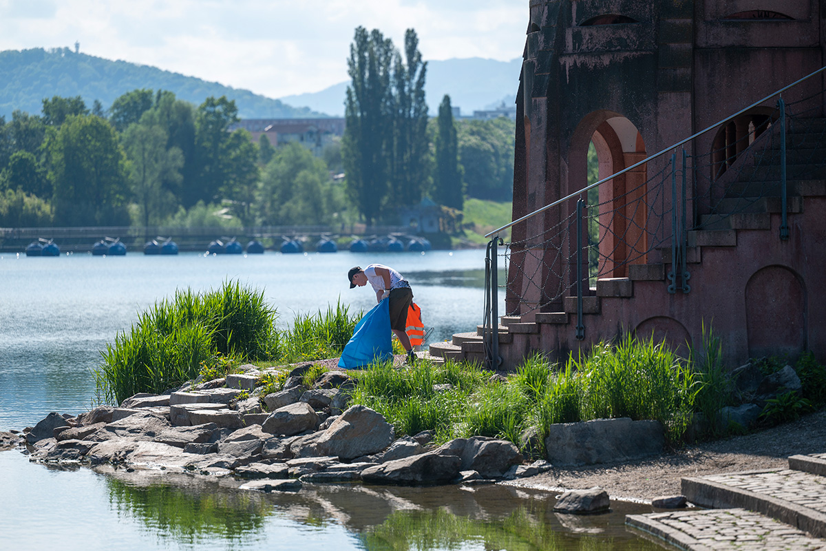 Junger Mann mit Müllsack beim Müllsammeln an einem Pavillon am See