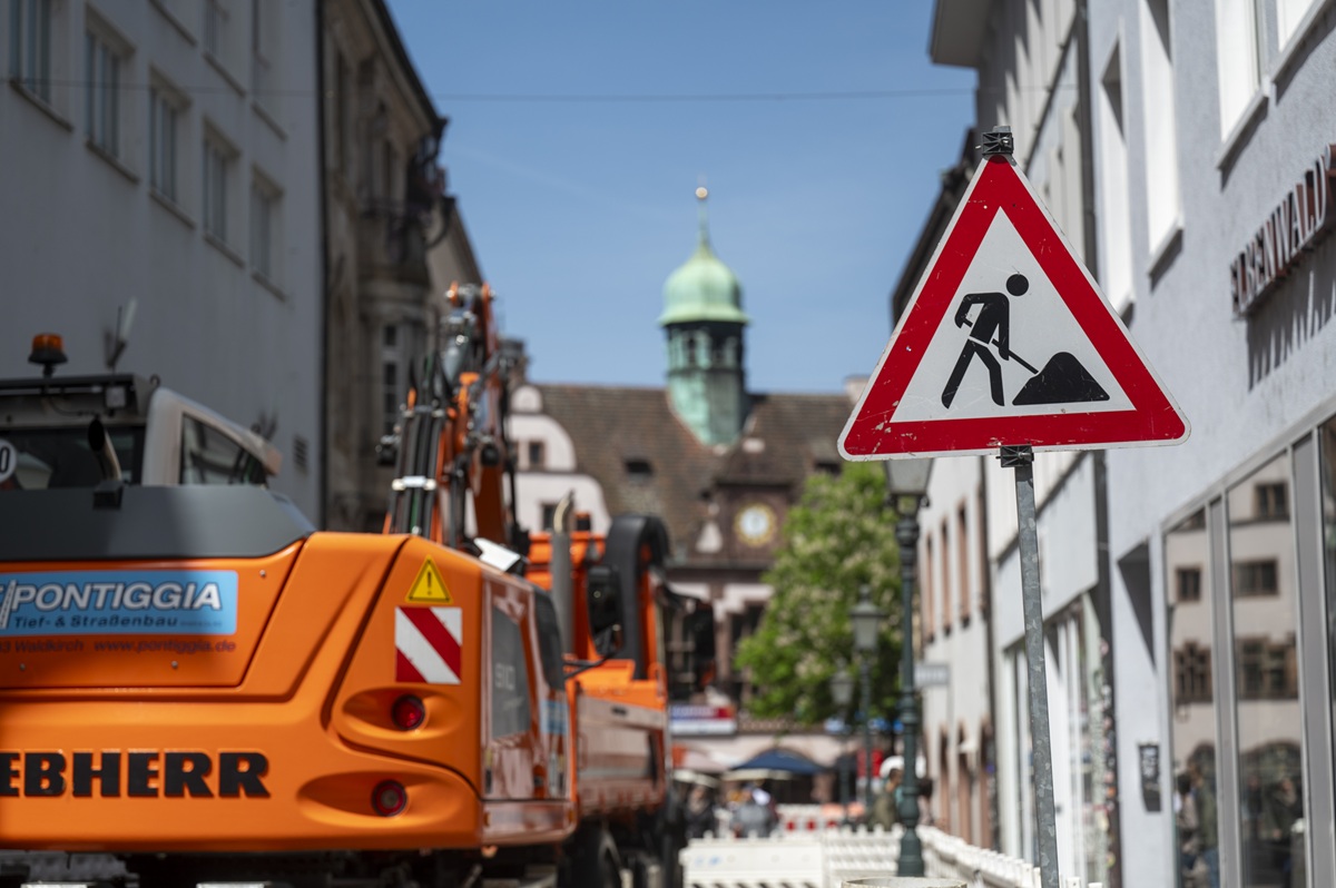 Ein orangener Bagger steht in der Rathausgasse, nebendran ein Baustellenschild. Im Hintergrund das Rathaus.