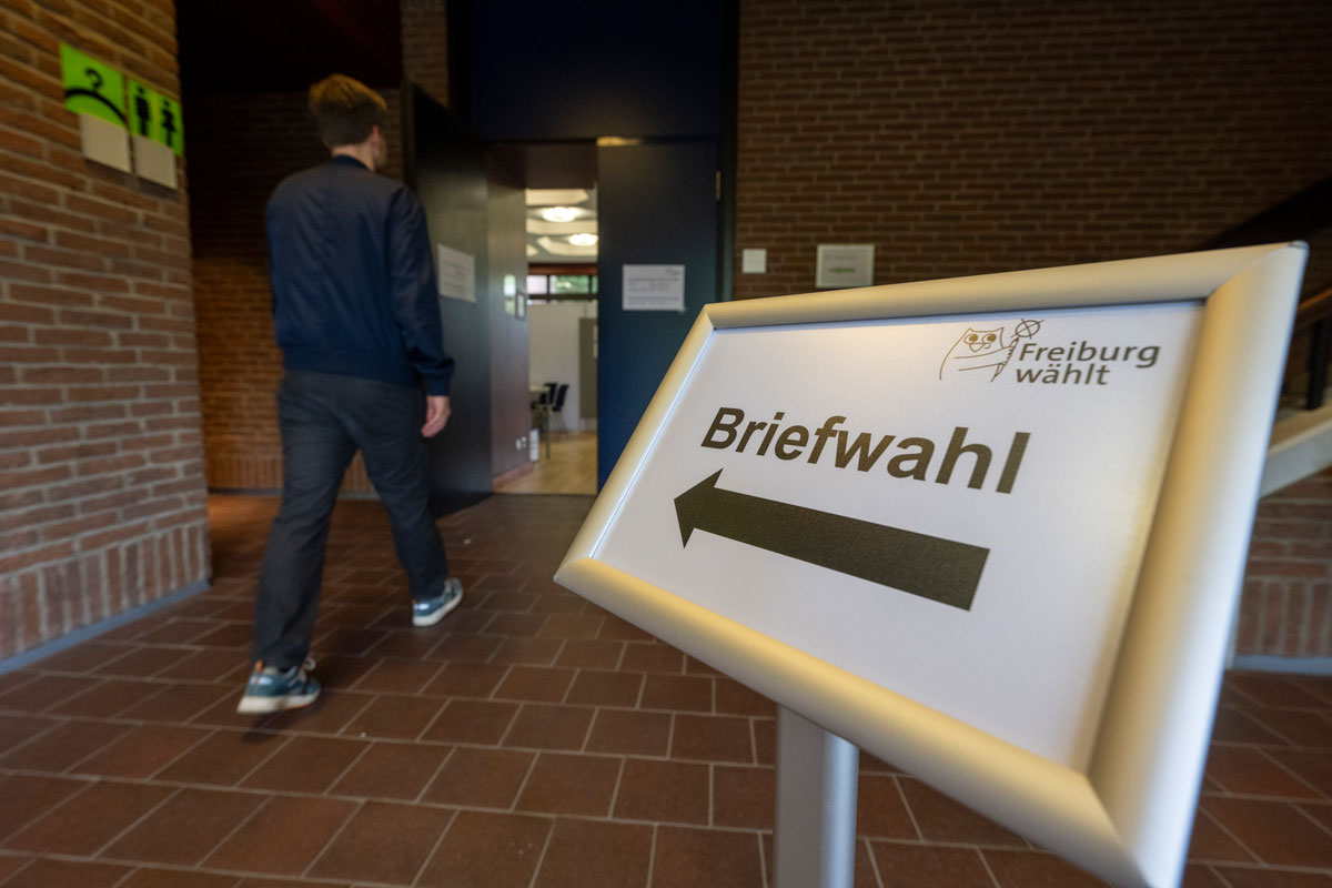 Schild auf dem Briefwahl steht; Person, die daran vorbei läuft