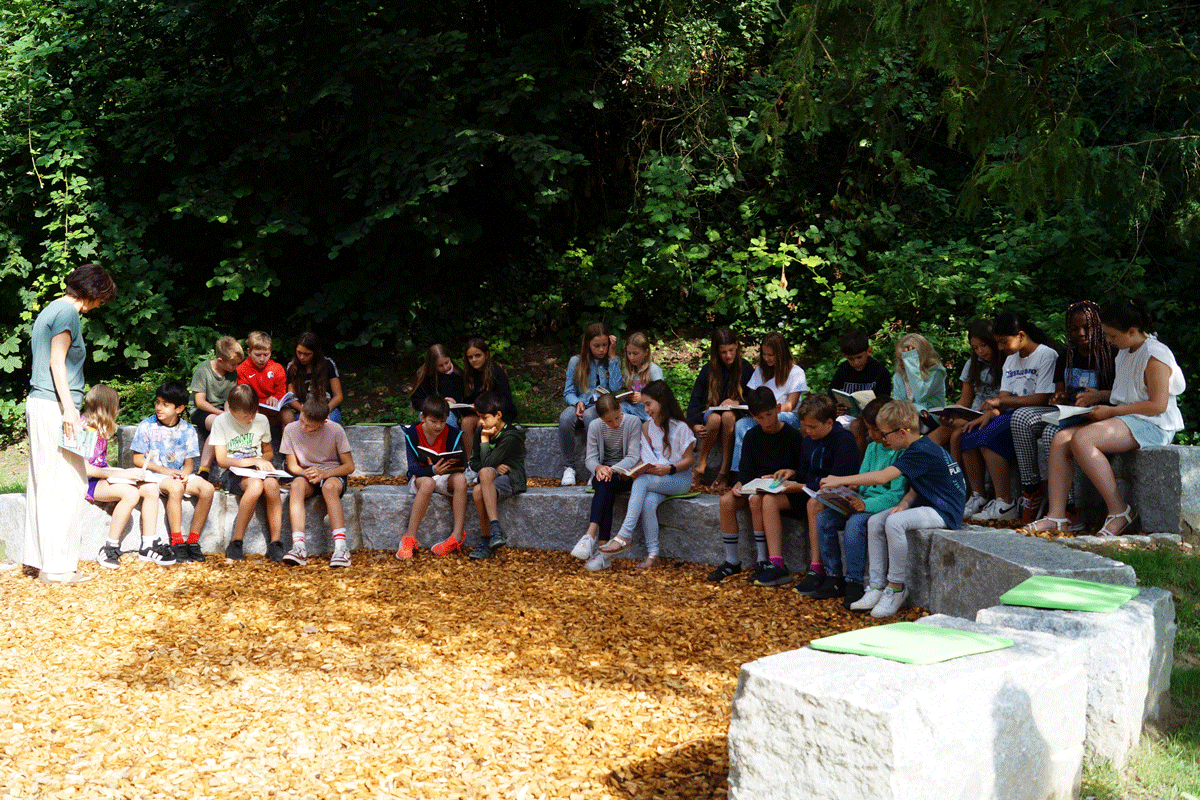 Viele Kinder sitzen in der Natur und sind am Lesen