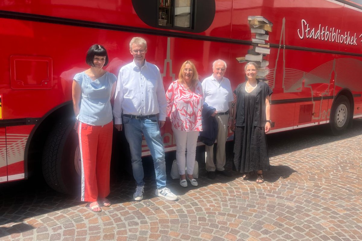 Fünf Personen stehen vor dem roten Bücherbus der Stadt Freiburg.