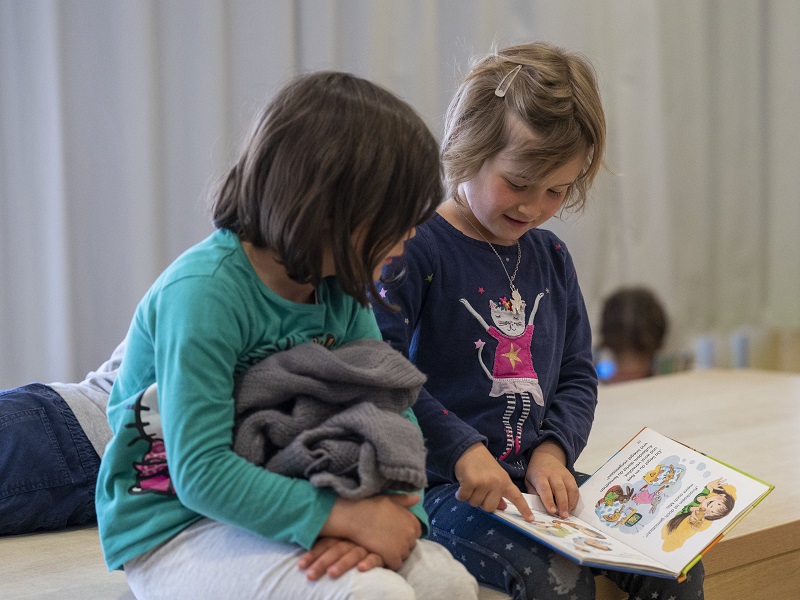 Zwei Mädchen schauen sich gemeinsam ein Bilderbuch an.