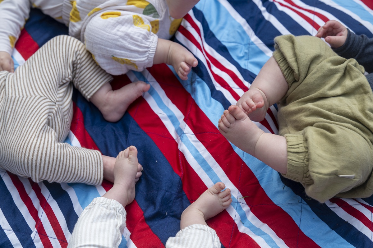 Vier paar Babyfüße auf einem Teppich.