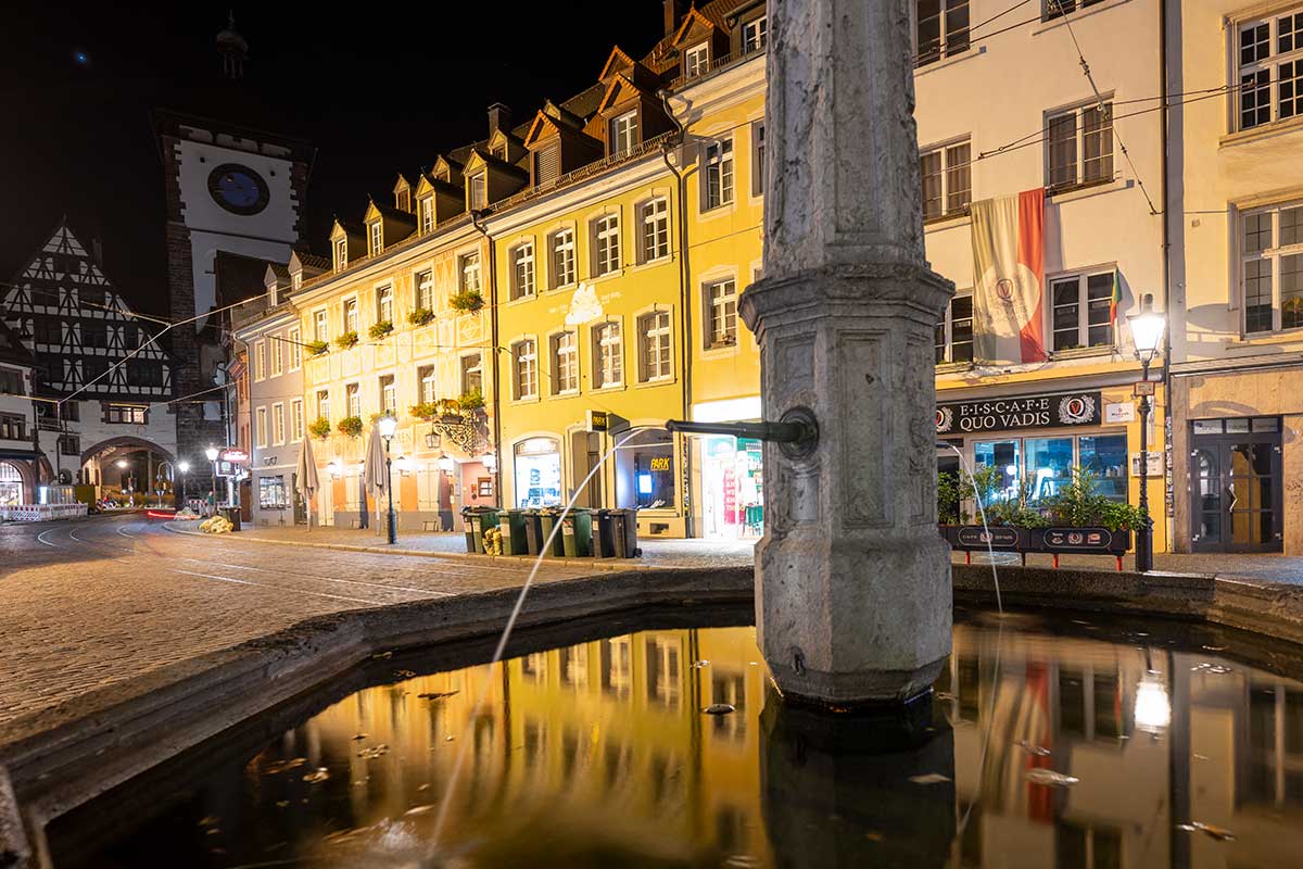 Oberlindenbrunnen mit dunklen Häusern und Licht im Hintergrund