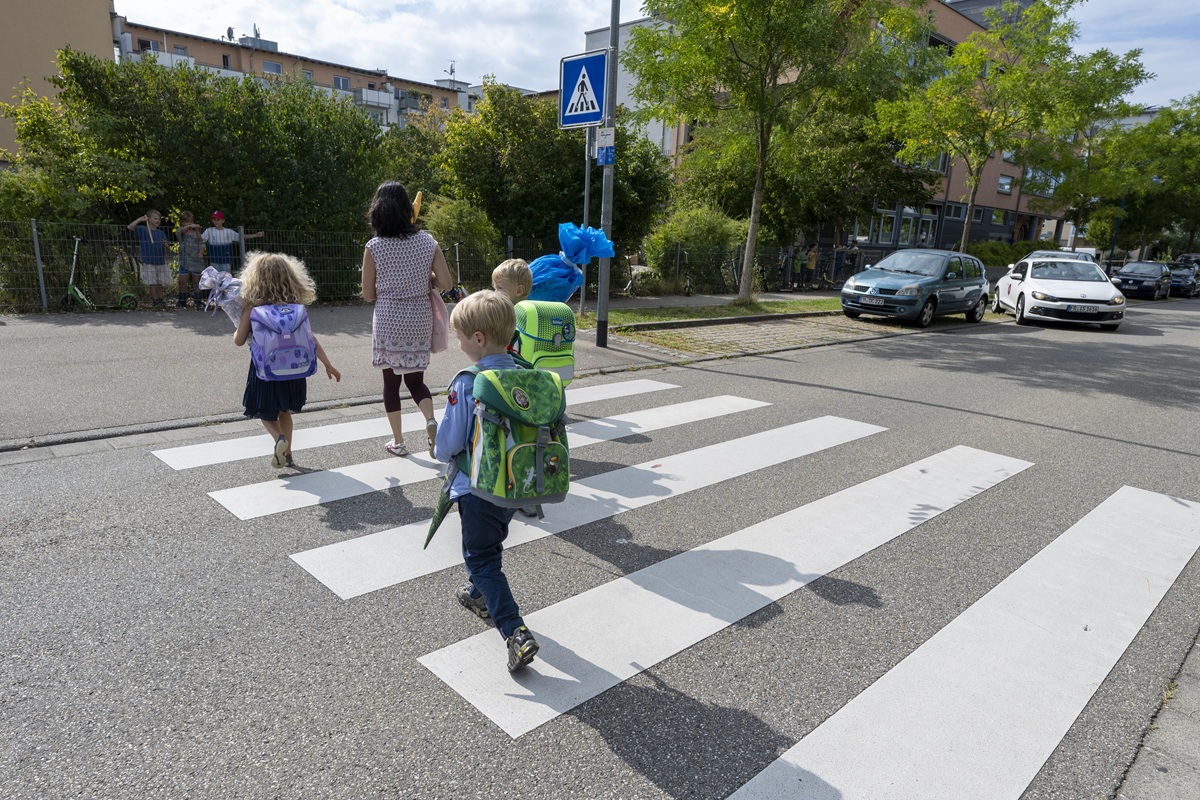 Zwei Kinder mit Schulranzen und eine erwachsene Person laufen über einen Zebrastreifen.