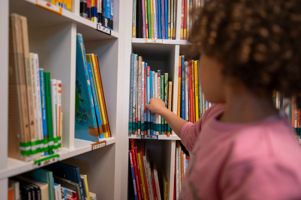 Ein Mädchen zieht ein Bilderbuch aus einem Bücherregal