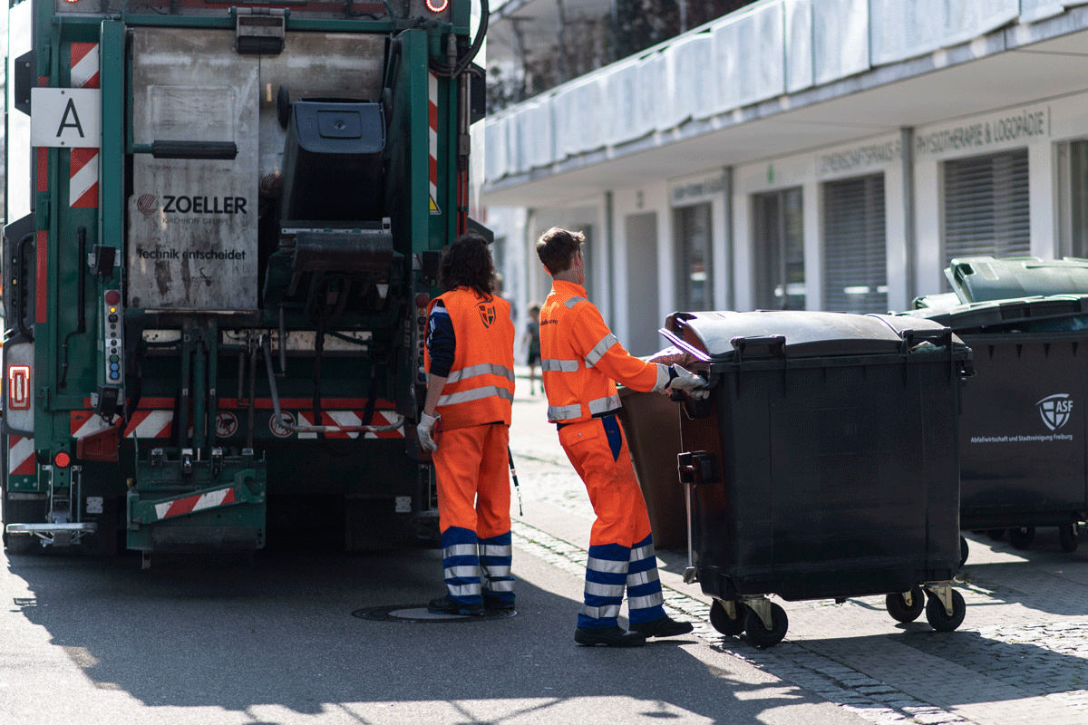 Zwei Personen fahren mit einem Müllauto