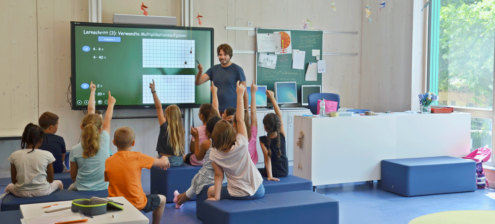 Schulklasse mit gehobenen Zeigefingern vor einem großen Bildschirm. (Foto: A. J. Schmidt)