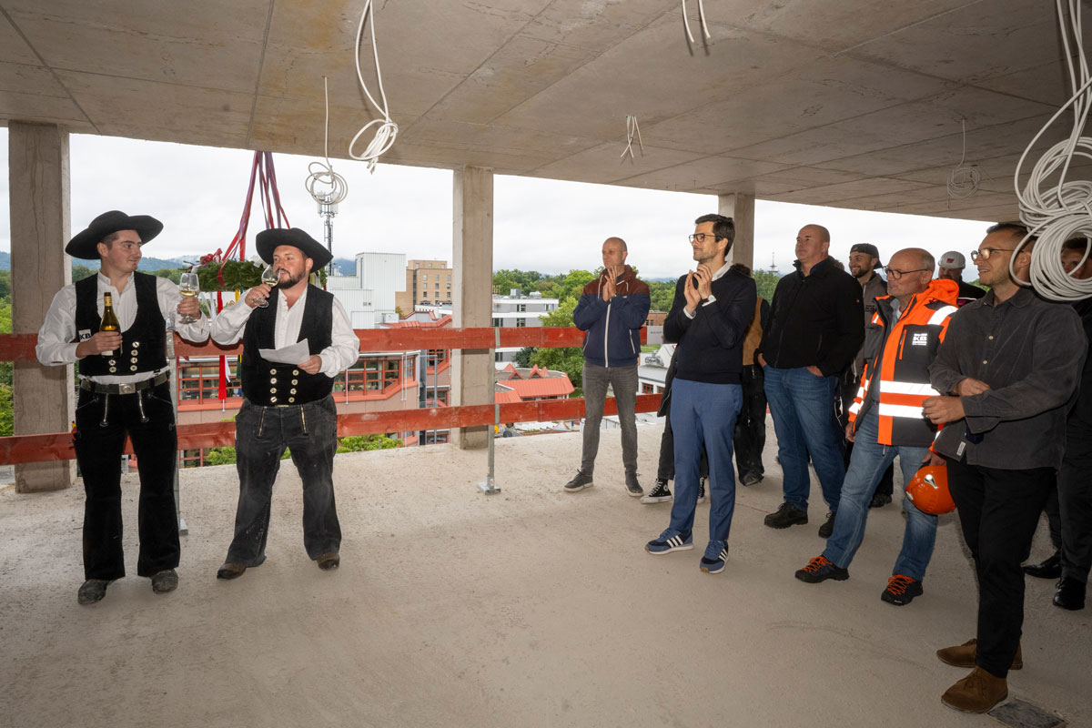 Richtfest: Links zwei Handwerker, rechts ein Publikum