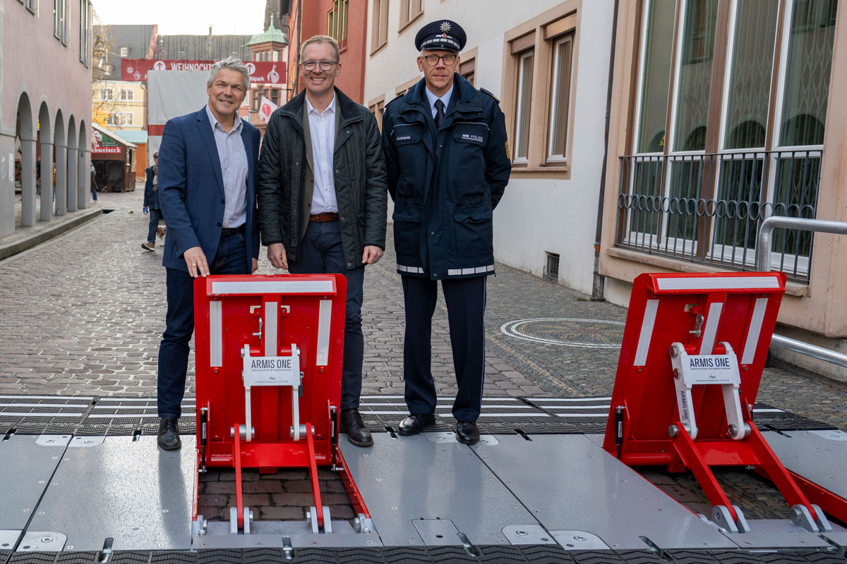 Drei Personen stehen hinter einer Sicherheitssperre