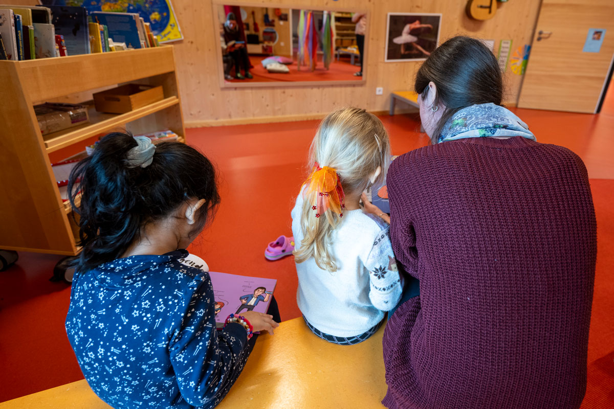 Zwei Kinder lesen mit einer Erzieherin