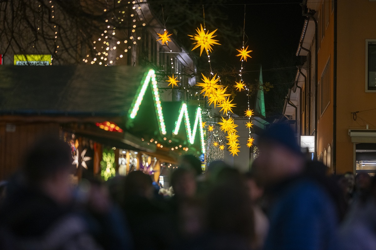Weinachtsmarkt mit beuleuchtenten Ständen und unscharfen Menschen im Hintergrund